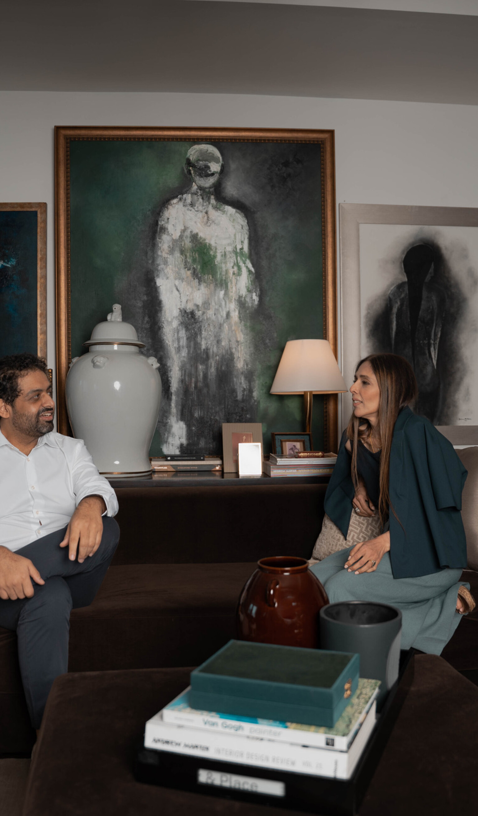 Bushra Khokhar and Tariq Ismail seated in conversation in a collected living space, artwork on the wall behind them