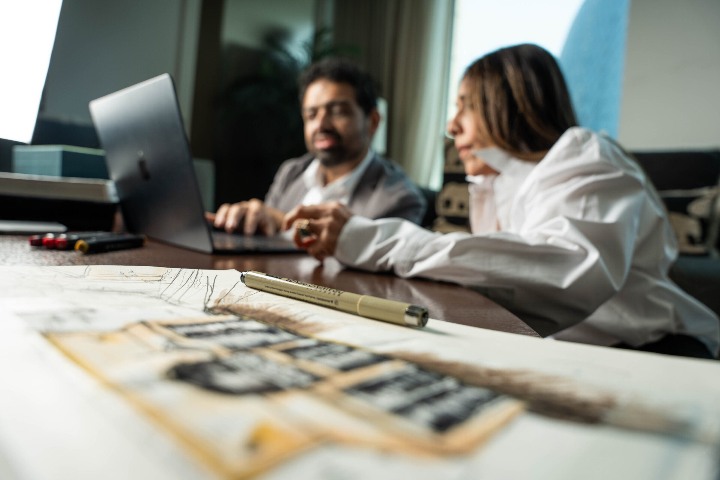 Bushra Khokhar and Tariq Ismail working through a project brief at a studio desk, a laptop open over drawings
